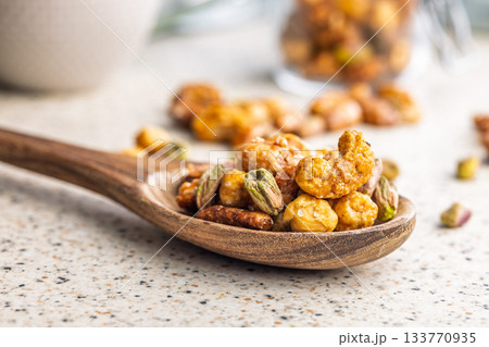 Nuts coated in sugar glaze on wooden spoon on kitchen table. 133770935