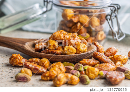 Nuts coated in sugar glaze on wooden spoon on kitchen table. 133770936