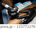 Hands of tattoo artist in black gloves busy with work. 133771270