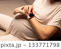 Pregnant woman with watches. Pregnant woman looking at her watches. 133771798