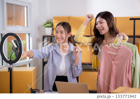 Two young asian woman live streaming online clothing store while showing clothing with smartphone. Two young asian woman live streaming online clothing store while showing clothing with smartphone. 133771942