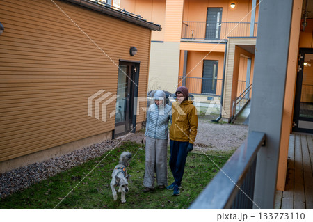 couple walking dog together in modern residential courtyard on cold autumn day couple walking dog together in modern residential courtyard on cold autumn day 133773110