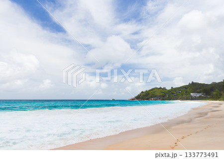 Sunlit tropical beach with clear turquoise waves, soft sand, and distant green hills Sunlit tropical beach with clear turquoise waves, soft sand, and distant green hills 133773491
