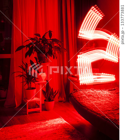 A long-exposure photograph that captures the pathway of a moving red light source in a dimly lit room 133773881