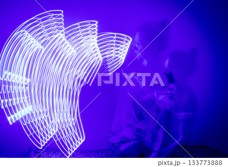 A long-exposure photograph that captures the pathway of a moving blue light source in a dimly lit room A long-exposure photograph that captures the pathway of a moving blue light source in a dimly lit room 133773888