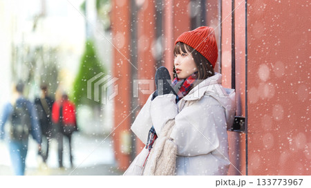 雪の降る冬の街角に立つ女性 133773967