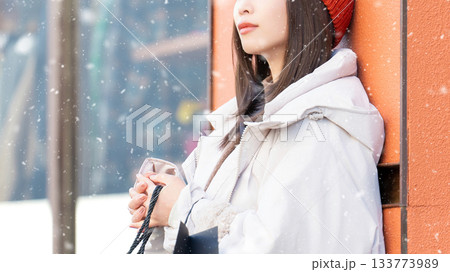 雪の降る冬の街角に立つ笑顔の女性 133773989