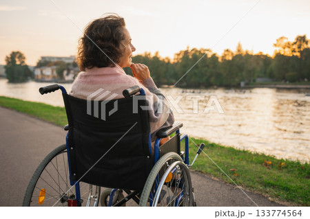 Sad senior woman sitting in wheelchair walking on road in city outdoor, back view. Old paralyzed lady in chair for people with disability feel depressed. Lonely elderly sick woman sits on wheelchair Sad senior woman sitting in wheelchair walking on road in city outdoor, back view. Old paralyzed lady in chair for people with disability feel depressed. Lonely elderly sick woman sits on wheelchair 133774564