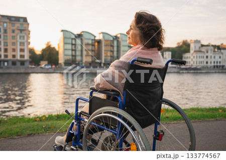 Sad senior woman sitting in wheelchair walking on road in city outdoor, back view. Old paralyzed lady in chair for people with disability feel depressed. Lonely elderly sick woman sits on wheelchair Sad senior woman sitting in wheelchair walking on road in city outdoor, back view. Old paralyzed lady in chair for people with disability feel depressed. Lonely elderly sick woman sits on wheelchair 133774567