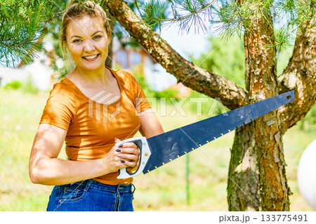 Female cuts branches of tree, using saw Female cuts branches of tree, using saw 133775491