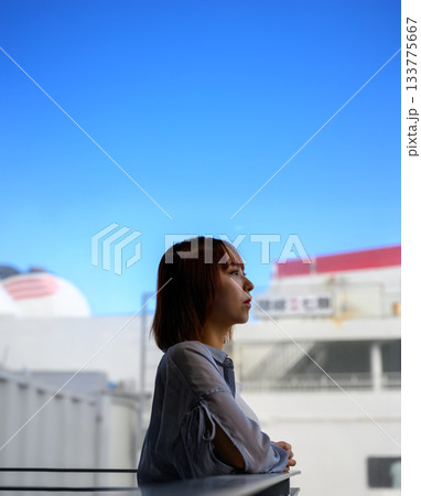 窓辺で外を眺める若い女性の横顔、明るい空と建物 133775667