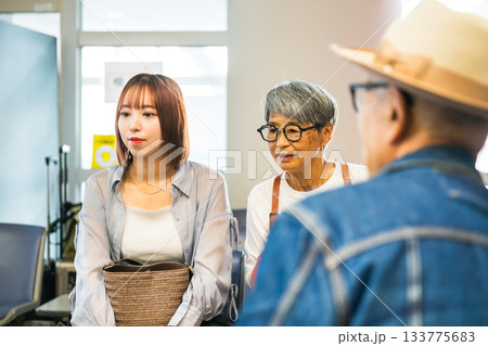 病院の待合室で年配のカップルと話す若い女性 病院の待合室で年配のカップルと話す若い女性 133775683