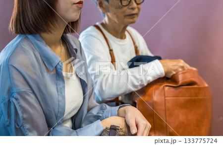 異なる世代の二人が並んで座り、荷物を見つめる 133775724