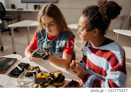 High school students working on robotics project, using online AI app to answer questions. 133775857