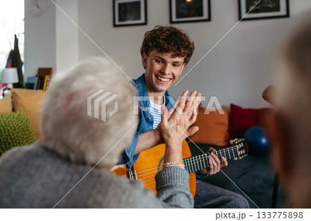Young musician volunteer playing guitar for senirors in retirement home. Young musician volunteer playing guitar for senirors in retirement home. 133775898