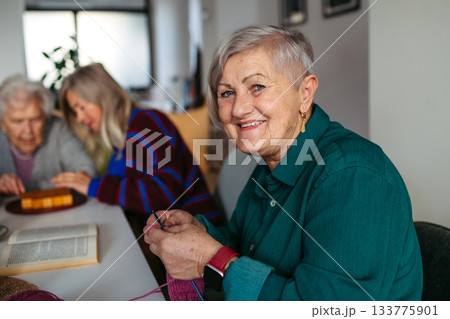 Group of senior people learning knitting together with caregiver tutor in a community center. 133775901