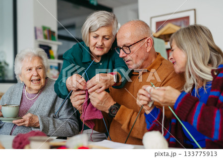 Group of senior people learning knitting together with caregiver tutor in a community center. 133775913
