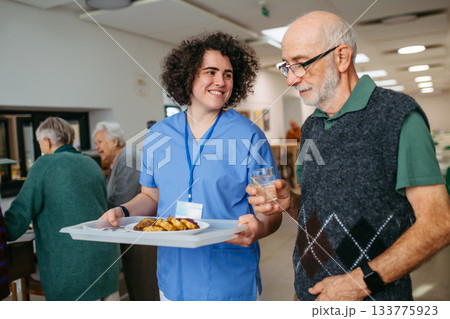 Senior man having lunch with supportive caregiver in community center cafeteria. Senior man having lunch with supportive caregiver in community center cafeteria. 133775923