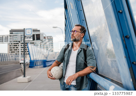 Bearded man with ball under arm waiting for bus. 133775987