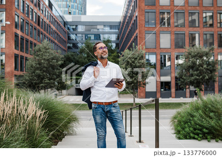 Businessman in front of office building, holding tablet and reading something. 133776000