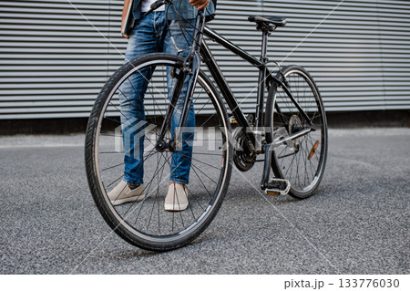City commuter riding bike on street, holding ball and headphones. 133776030