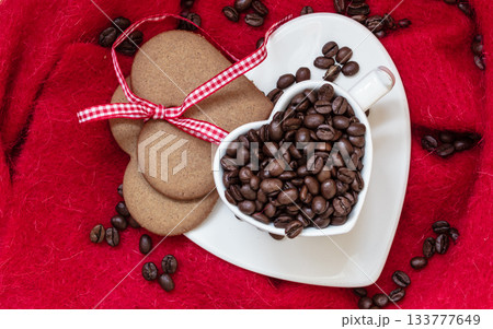 Coffee beans in heart shaped cup and dessert on red 133777649