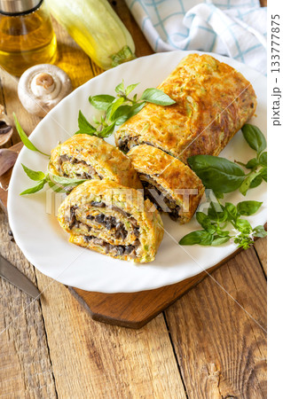 Zucchini roll with mushroom filling and herbs served on a white plate on a rustic table. Zucchini roll with mushroom filling and herbs served on a white plate on a rustic table. 133777875