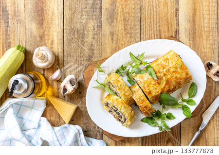 Zucchini roll with mushroom filling and herbs served on a white plate on a rustic table. Top view. Zucchini roll with mushroom filling and herbs served on a white plate on a rustic table. Top view. 133777878