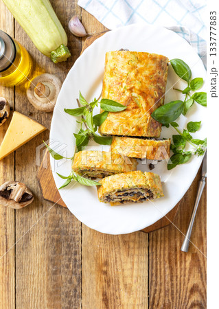 Zucchini roll with mushroom filling and herbs served on a white plate on a rustic table. Top view. Zucchini roll with mushroom filling and herbs served on a white plate on a rustic table. Top view. 133777883