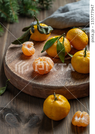 Whole and peeled tangerines with green leaves on a round wooden board Whole and peeled tangerines with green leaves on a round wooden board 133777947