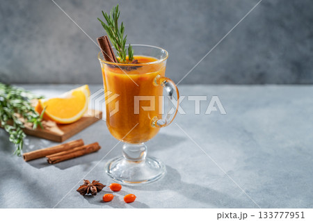 Sea buckthorn herbal tea in a glass on a blue background with orange, spices, and shadow. 133777951
