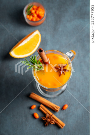 Sea buckthorn herbal tea in a glass on a dark background with berries, spices 133777955