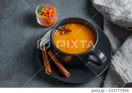 Sea buckthorn tea in a black cup on a dark background with berries, spices and napkin. 133777956