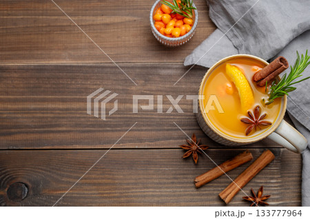 Sea buckthorn herbal tea in a cup on a wooden background with spices, berries and napkin Sea buckthorn herbal tea in a cup on a wooden background with spices, berries and napkin 133777964