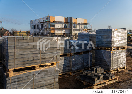 Pallets of gray paving stones wrapped in plastic on a dirt ground 133778454