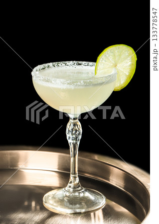 Elegant margarita cocktail in a crystal coupe glass with salt rim and fresh lime slice, isolated on black background, perfect for bar menus, beverage branding, cocktail advertising Elegant margarita cocktail in a crystal coupe glass with salt rim and fresh lime slice, isolated on black background, perfect for bar menus, beverage branding, cocktail advertising 133778547