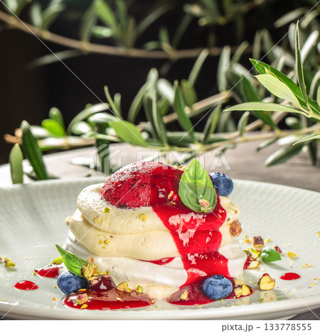 Gourmet pavlova dessert topped with vibrant berry coulis, fresh blueberries and pistachios Gourmet pavlova dessert topped with vibrant berry coulis, fresh blueberries and pistachios 133778555