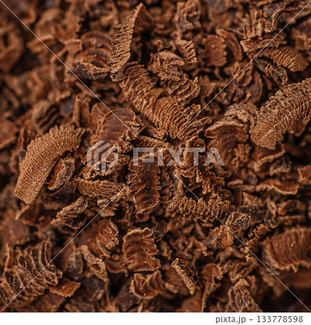 Close-up macro texture of finely grated chocolate shavings showing rich curls, detailed surface patterns and deep cocoa tones, perfect as a dessert background, confectionery design element 133778598