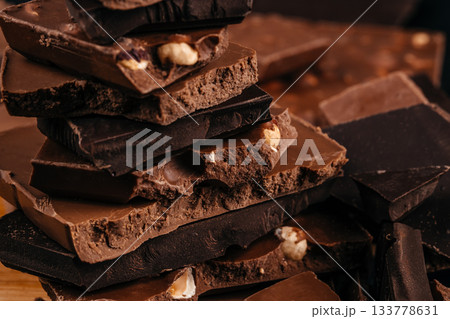 Stacked assortment of broken dark and milk chocolate pieces with nuts and porous textures, captured in warm macro lighting premium confectionery advertising, dessert branding Stacked assortment of broken dark and milk chocolate pieces with nuts and porous textures, captured in warm macro lighting premium confectionery advertising, dessert branding 133778631