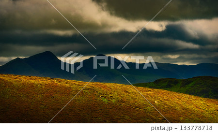 Dramatic landscape with rolling green hills under a stormy sky. Dramatic landscape with rolling green hills under a stormy sky. 133778718