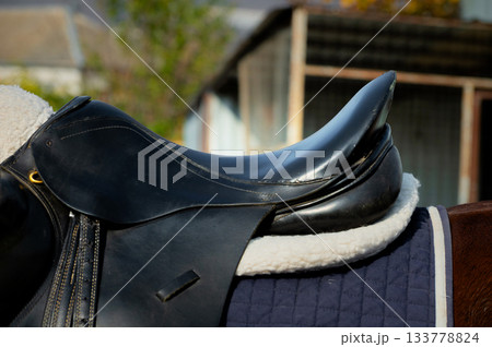 Close up of a sport horse saddle. Quality classical leather saddle ready for horse workout. Equestrian sport background outdoors 133778824