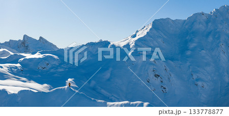 Aerial photo of a ski mountaineer standing on a snowy alpine ridge in Austria. Winter landscape, backcountry adventure, clear blue sky with sunshine and solitude in breathtaking mountain scenery. Aerial photo of a ski mountaineer standing on a snowy alpine ridge in Austria. Winter landscape, backcountry adventure, clear blue sky with sunshine and solitude in breathtaking mountain scenery. 133778877