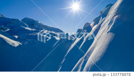 Aerial photo of a ski mountaineer standing on a snowy alpine ridge in Austria. Winter landscape, backcountry adventure, clear blue sky with sunshine and solitude in breathtaking mountain scenery. 133778878