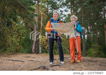 Hiking tourism. Senior couple man woman looking track in paper map enjoying hiking in forest. Happy old people backpackers hikers enjoy walking hike trekking tourism active vacation beauty of nature Hiking tourism. Senior couple man woman looking track in paper map enjoying hiking in forest. Happy old people backpackers hikers enjoy walking hike trekking tourism active vacation beauty of nature 133778987