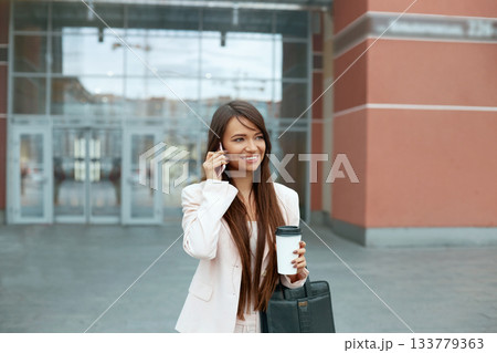 Business Woman With Phone Near Office. Portrait Of Beautiful Smiling Female Talking On Phone While Standing Outdoors. Phone Communication. Business Woman With Phone Near Office. Portrait Of Beautiful Smiling Female Talking On Phone While Standing Outdoors. Phone Communication. 133779363