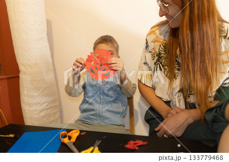 Child presenting handmade paper snowflake to adult 133779468