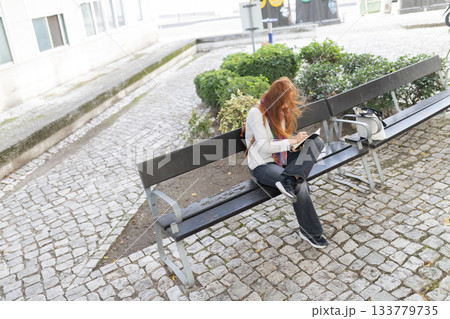 Young woman writing notes in urban park bench Young woman writing notes in urban park bench 133779735