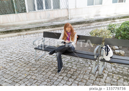 Adult woman writing notes in outdoor park bench Adult woman writing notes in outdoor park bench 133779736