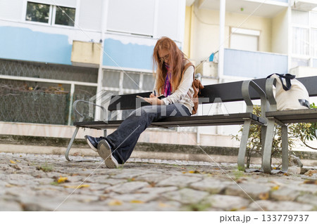 Woman with red hair writing diary on urban bench Woman with red hair writing diary on urban bench 133779737