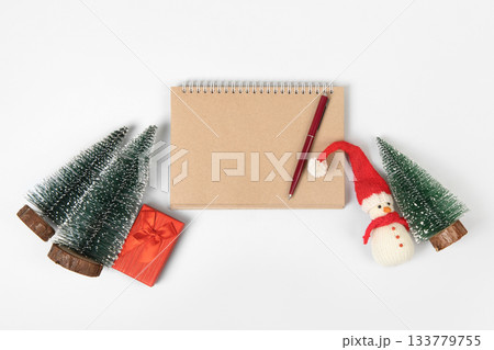 Christmas composition of snowman toy, gift box and toys on Christmas tree, with open blank notebook and pen on gray background for writing goals and plans for the New Year. Flat lay, copy space Christmas composition of snowman toy, gift box and toys on Christmas tree, with open blank notebook and pen on gray background for writing goals and plans for the New Year. Flat lay, copy space 133779755
